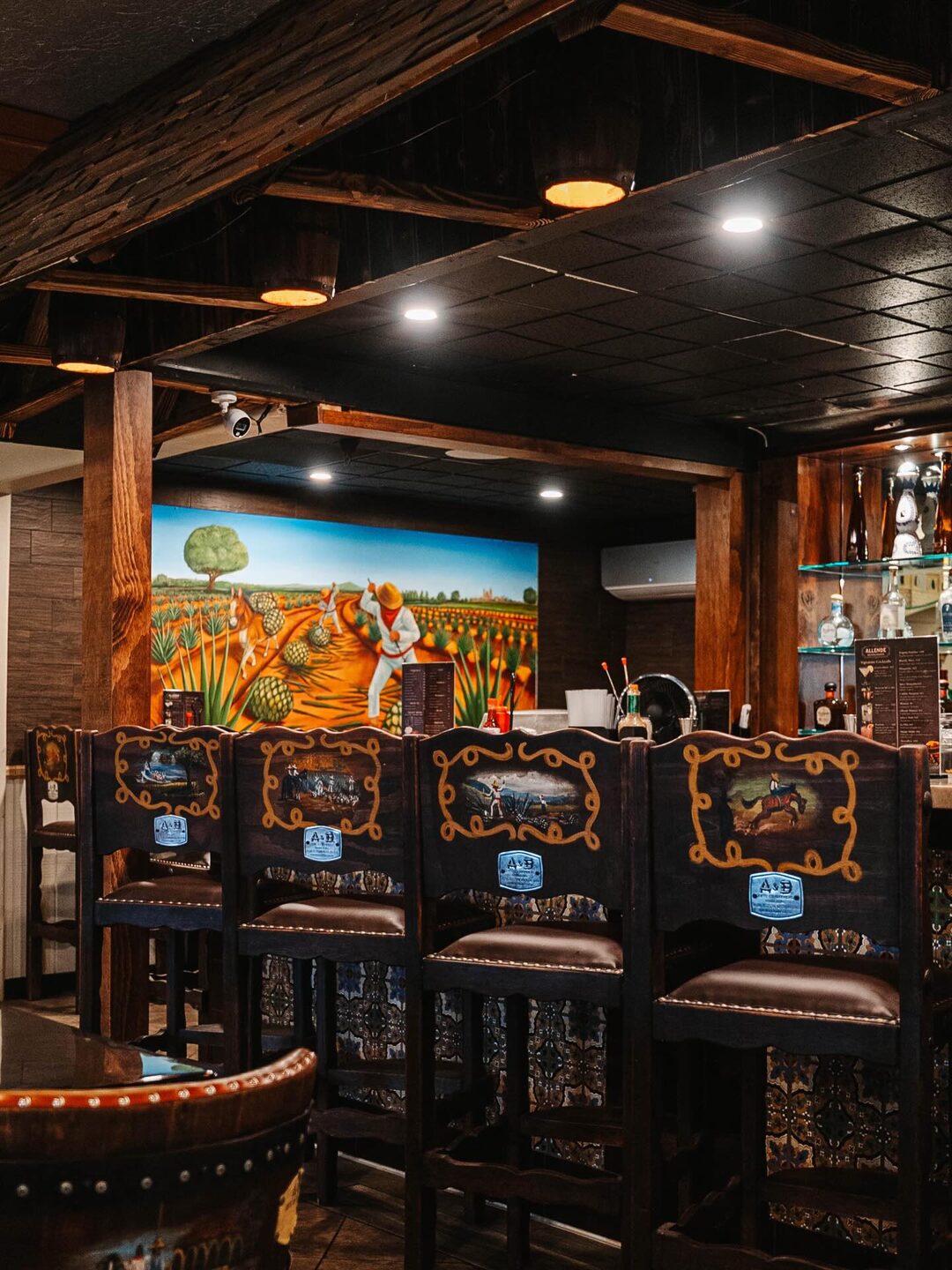 Su bar: sillas pintadas a mano, traídas de Josefino de Allende, frente a un mural de campos de agave